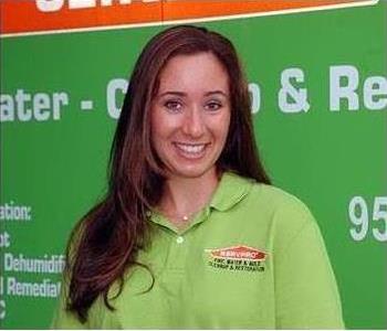 Female employee smiling in front of a green SERVPRO vehicle.