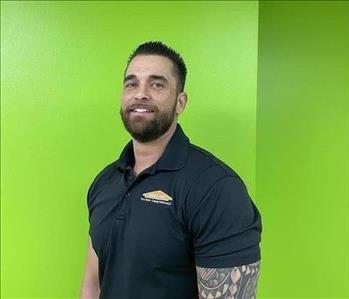 Male employee smiling with green wall background.
